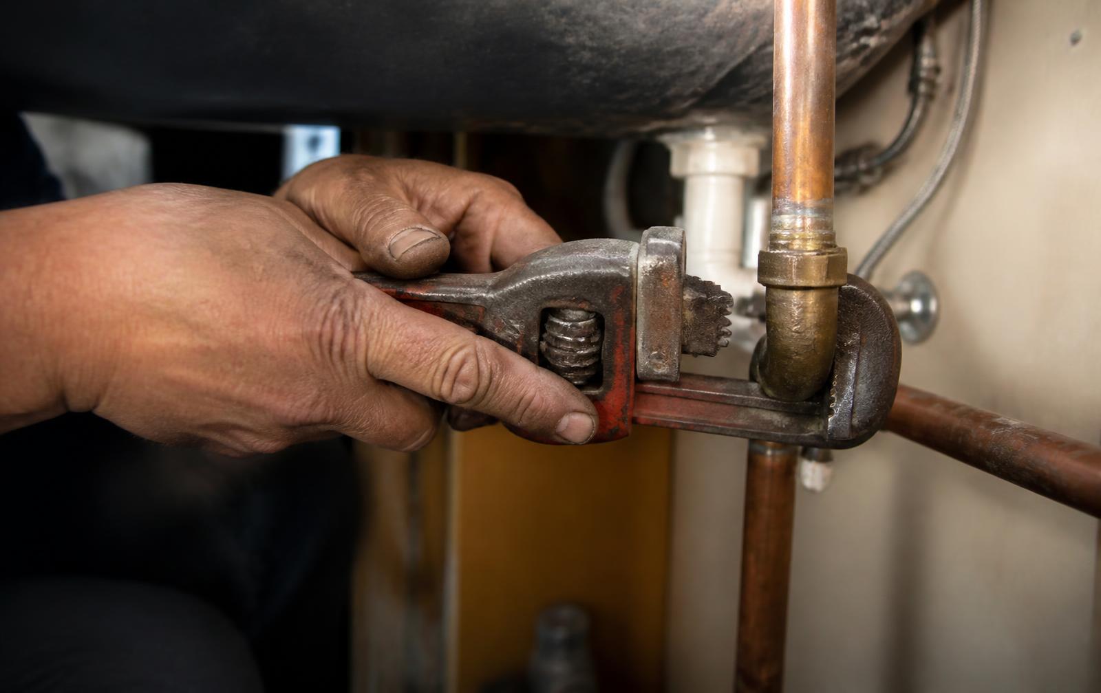 A contractor's hands doing hands-on plumbing work that AI cannot replace.